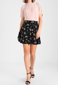 Haut rose clair à manches courtes avec un design plissé, associé à une jupe florale noire. La jupe présente de petites fleurs blanches, jaunes et vertes.