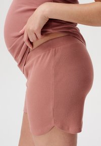 Zbliżenie osoby podnoszącej prążkowaną różową bluzkę, aby odsłonić dopasowane prążkowane różowe spodenki o wysokim stanie z falbaniastym wykończeniem.