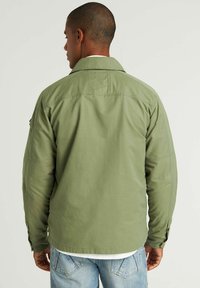 Olijfgroene jack met een gestructureerde silhoutte, voorzien van een gespreid kraag, drukknoopsluiting en zijzakken. Lichtgewicht stof met een gladde textuur.