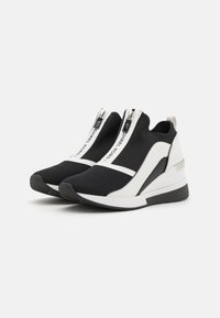 Sneaker slip-on in bianco e nero con tomaia in mesh testurizzato, dettagli in pelle liscia, zip frontale e suola a cuneo sollevata.