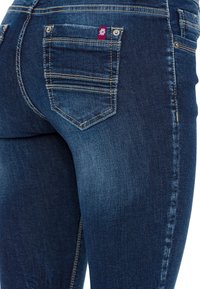 Donkerblauwe denim jeans met een slim fit ontwerp, voorzien van een verhoogd achterzak met een rood label en subtiele stiksels langs de zijkanten.