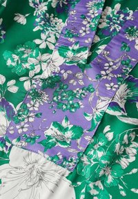 Tessuto floreale in tonalità di verde e viola con contorni bianchi, caratterizzato da una superficie liscia e motivi floreali sovrapposti.