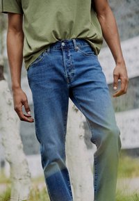 Blauwe denim jeans met een relaxte pasvorm, voorzien van een klassieke vijfzakkenontwerp en knoopsluiting, gecombineerd met een groene t-shirt.