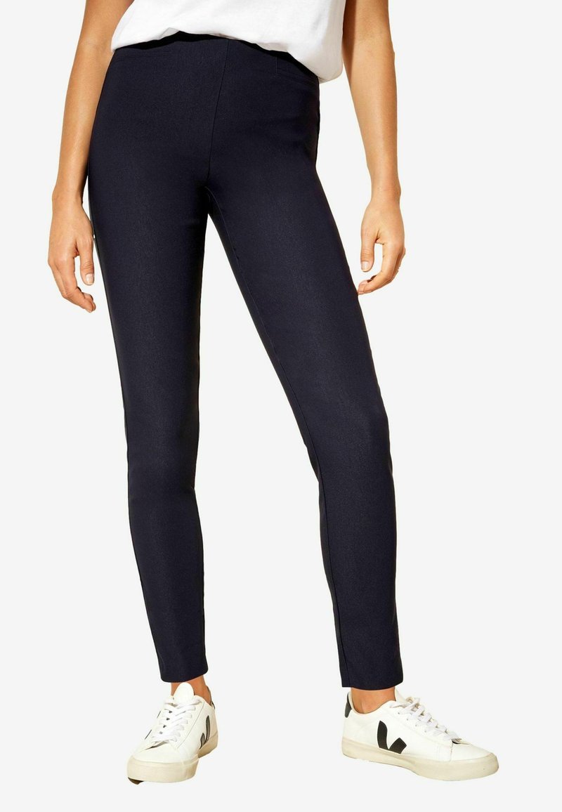Leggings extensibles bleu marine au design épuré, en tissu texturé et avec une taille haute, associés à des baskets blanches avec des accents noirs.