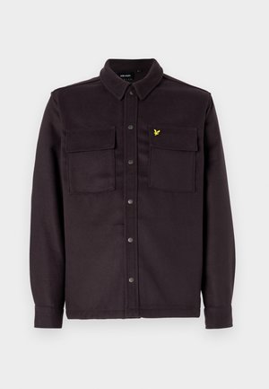 Chemise-jetée à boutons de couleur violet foncé, fabriquée en tissu à finition texturée, avec deux poches poitrine et un petit logo jaune.