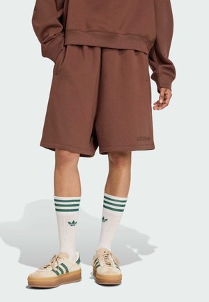 Sudadera marrón con pantalones cortos a juego, tejido texturizado, corte holgado. Calcetines blancos con rayas verdes, zapatos beige con detalles verdes.