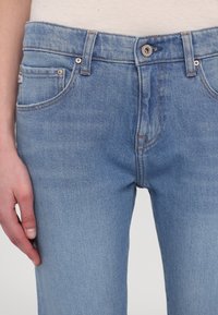 Średniopisane niebieskie dżinsy w jasnym denimu, z przednimi kieszeniami, subtelnym przeszyciem i klasycznym pięciokieszeniowym fasonem. Guziki w srebrnym odcieniu.