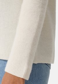 Cremfarbener Strickpullover mit gerippter Textur, im lässigen Schnitt und mittellangen Ärmeln, kombiniert mit hellblauen Jeans.