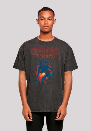 Black oversized t-shirt featuring "Stranger Things" graphic in red and blue, with a textured, worn look and distinct collar and sleeve design.