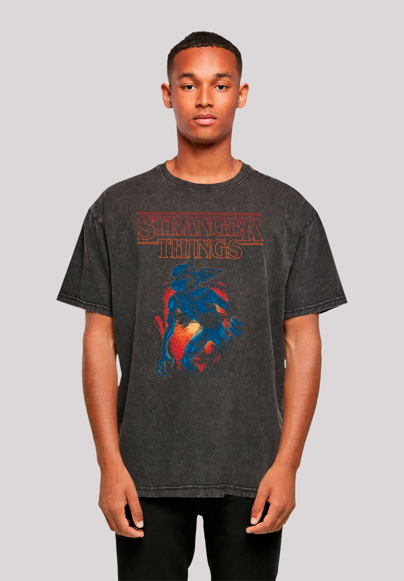 Black oversized t-shirt featuring "Stranger Things" graphic in red and blue, with a textured, worn look and distinct collar and sleeve design.