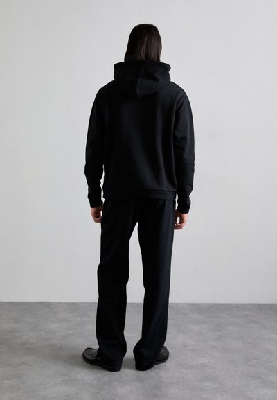 Sudadera de algodón negra con una capucha grande, combinada con pantalones negros. Diseño sencillo, corte relajado, textura suave, detalles mínimos y sin patrones visibles.