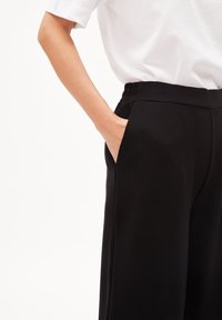 Svarta vida byxor med elastisk midja och sidofickor, kombinerade med en vit topp med korta ärmar. Slät tygtextur.