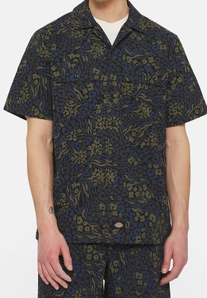 Short-sleeve button-up shirt with navy, olive, and black abstract leopard print worn over a white t-shirt.