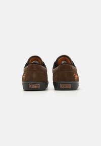 Sapatilhas de skate em camurça castanha com detalhes pretos e forro interior laranja. Apresentam uma sola grossa preta e o logótipo da Etnies no calcanhar.