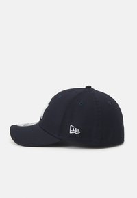 Navy baseball cap with a curved brim, featuring a white logo on the front and a small white brand tag on the side. Cotton material, six panels.