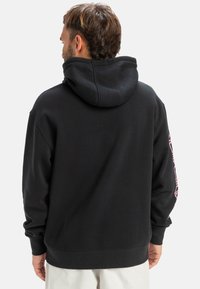 Black hooded sweatshirt with a soft texture, featuring a large hood and pink graphics on the sleeves. Ribbed cuffs and hem.