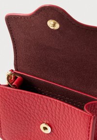 Červená kožená peněženka s texturovaným povrchem, zvlněným horním okrajem, zapínáním na zlatý druk a měkkým semišovým vnitřkem s malým přihrádkou.