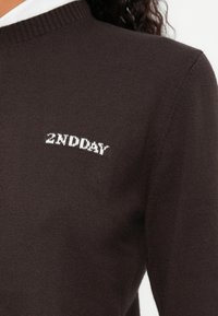 Pull en tricot marron présentant un col rond et un logo textuel blanc "2NDDAY" subtilement affiché sur la poitrine.