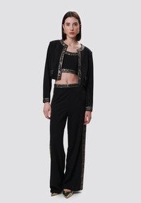 Zwarte tweedelige outfit met een cropped jack en hoge taille broek, versierd met metalen accenten en een gestreepte rand. Gelaagd textiel.