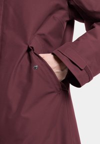 Burgundy vattentät jacka med sidoficka med tryckknappsstängning och en strukturerad mudd; slätt tyg med en minimalistisk design.