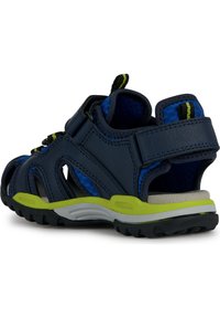 Las sandalias azul marino presentan un diseño transpirable con cortes, acentos en verde lima y correas ajustables para un ajuste seguro. Suela de goma texturizada.