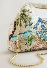 Sac à main en tissu beige avec broderie détaillée de palmiers, vagues et cabane de plage, orné de perles et d'une bandoulière en chaîne dorée.