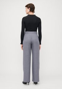 Zwarte blouse met lange mouwen en een kraag met kant, gecombineerd met grijze wijde broekspijpen. De outfit heeft een op maat gemaakt ontwerp en een soepele textuur.