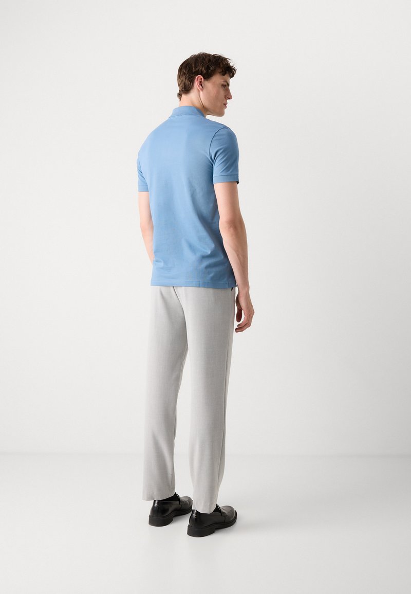 Camisa polo de manga corta azul claro combinada con pantalones grises claros y zapatillas negras. Se puede ver la tela suave y un ajuste entallado.