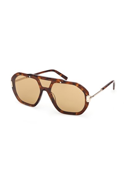 Lunettes de soleil épaisses à monture écaille de tortue avec de grandes verres teintés marron et des branches en métal doré, inclinées vers la droite sur un fond blanc.