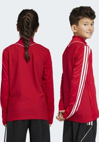 Rote Sportjacke mit strukturiertem, atmungsaktivem Design. Mit weißen Streifen an den Ärmeln, einem Reißverschlusskragen und leichtem Material ausgestattet.