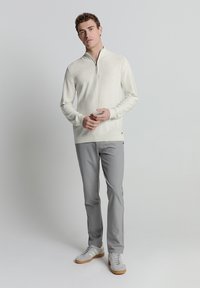 Lichtgekleurde pullover met een kwart-rits ontwerp, gecombineerd met grijze broek en grijze sneakers met witte accenten. Zachte textuur over de hele oppervlakte.