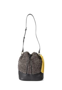 Bolso tipo bucket con cuerpo de piel sintética gris texturizada y base de cuero negro, que presenta un cierre de cordón y un acento de borlas amarillas.