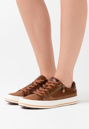 Hnědé tenisky s hladkým koženým povrchem, texturovanými doplňky, hnědými tkaničkami a ozdobným zipem. Bílá podrážka s světle hnědým pruhem.