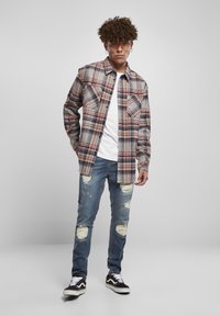 Rutig flanellskjorta i beige, blått och rött; två bröstfickor. Bärs över en vit T-shirt med slitna blåjeans och svarta sneakers.