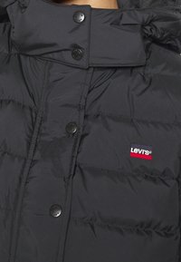 Black puffer jacket with quilted texture, snap buttons, and a branded Levi's logo patch in red, white, and blue near the neckline.
