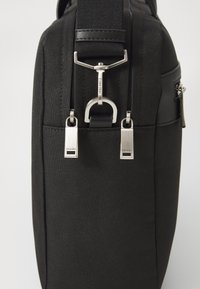 Sac à épaule en tissu noir avec une finition texturée, des zips et quincaillerie en métal argenté, et une bandoulière amovible pour des options de transport polyvalentes.