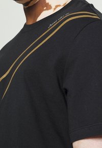 Detailní záběr osoby v černém tričku se zlatými diagonálními pruhy a textem "Just do it." blízko výstřihu.