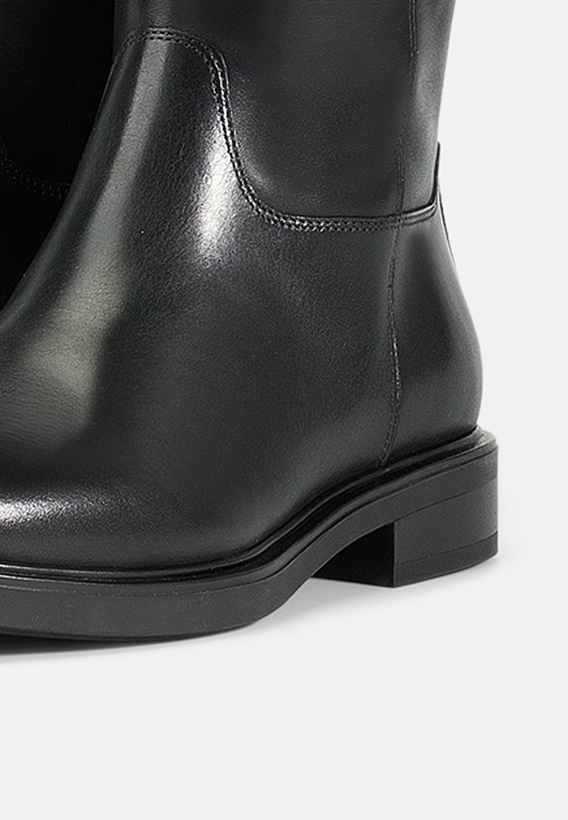 Bota de tobillo de cuero negro con un acabado suave, tacón bajo y detalles de costura mínimos a lo largo de los lados.