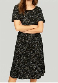 Svart klänning med korta ärmar, blommönster i vitt och gult, knälång, lös passform, lätt material, rundad halsringning.