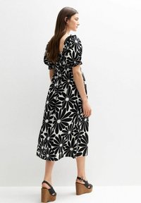 Zwart-wit bloemen maxi-jurk met puffmouwen en een geraffineerde buste, afgewerkt met een losvallende pasvorm en zichtbare textuur.