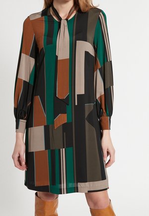 Jurk gemaakt van lichtgewicht stof met een striksluiting bij de hals. Voorzien van geometrische patronen in groen, bruin, beige en zwart. Lange mouwen met geplooide manchetten.