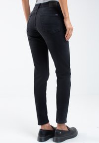 Vaqueros skinny de mezclilla negra con cintura media, cinco bolsillos y una textura suave. Presenta una cinturilla con marca y una silueta estilizada.