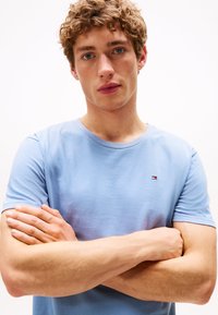 T-shirt azzurro chiaro a maniche corte in cotone, con un piccolo logo sul petto. Il tessuto sembra morbido e presenta un classico scollo rotondo.