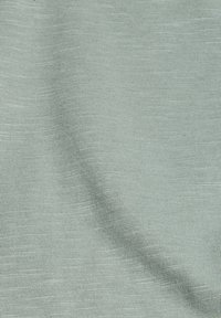 Gros plan sur un tissu doux vert clair montrant une texture fine tricotée et des plis doux.