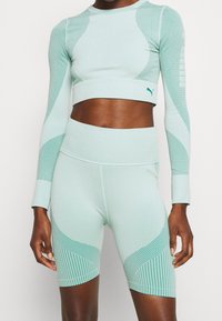 Helle mintgrüne Sportbekleidung bestehend aus einem verkürzten Langarm-Oberteil mit Netzdetails und hoch taillierten Shorts mit gestreiften und gepunkteten Mustern.