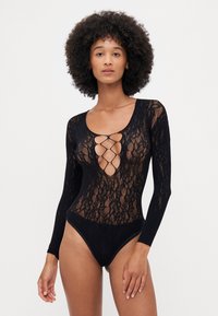 Body in pizzo nero con maniche lunghe, caratterizzato da un profondo scollo e dettagli incrociati sul davanti, ha una texture trasparente e un design aderente.
