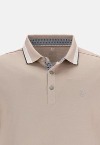 Polo shirt beige chiaro con un tessuto texturizzato, tre bottoni, colletto solido e interno del colletto decorato con un motivo che presenta dettagli neri.
