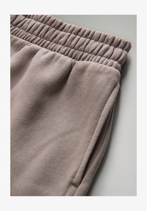 Light mauve joggers with a gathered elastic waistband, soft texture, and side pockets, showcasing a smooth, simple design.