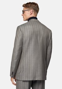Veste de costume à rayures grises avec col en marine contrastant, fermeture à un bouton et tissu texturé. Comprend deux poches arrière et des poignets à boutons.