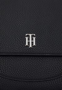 Borsa in pelle nera testurizzata con un logo metallico argento con lettere intrecciate, che conferisce un aspetto elegante e moderno.